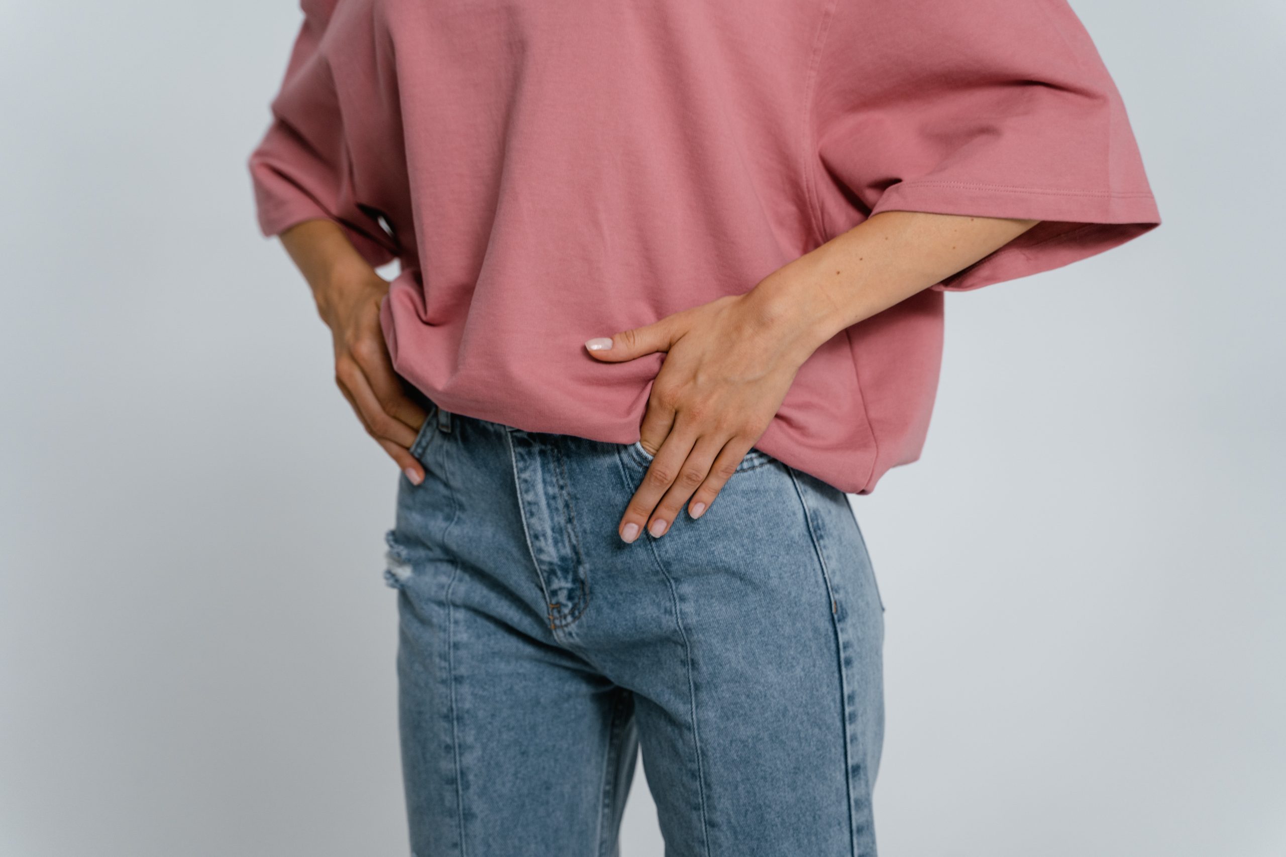Picture of a women's hips and torso. She is wearing a pink shirt and lightly coloured jeans.